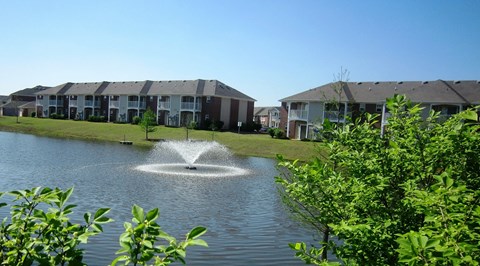 A fountain in the middle of a lake surrounded by greenery.