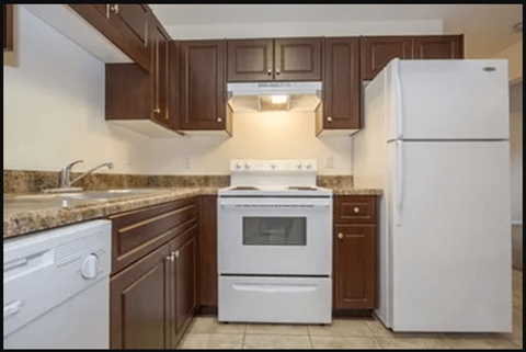A white refrigerator stands in a kitchen with brown cabinets.