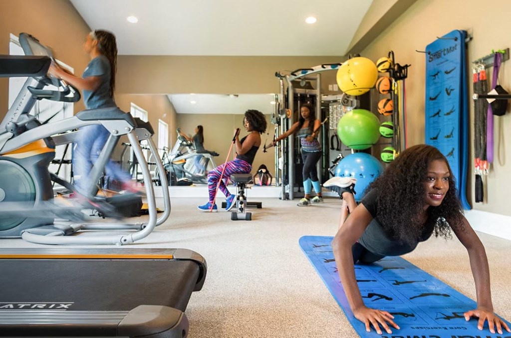 a woman does pushups in a gym while others exercise in the background