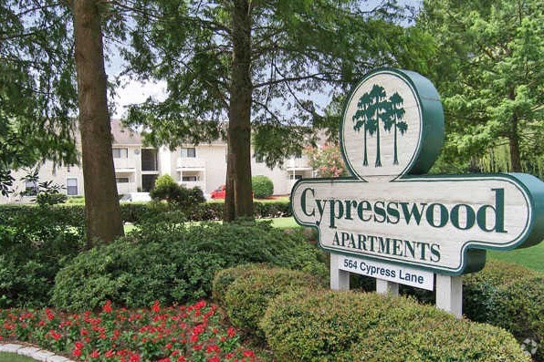 a sign for cypresswood apartments in front of trees and flowers