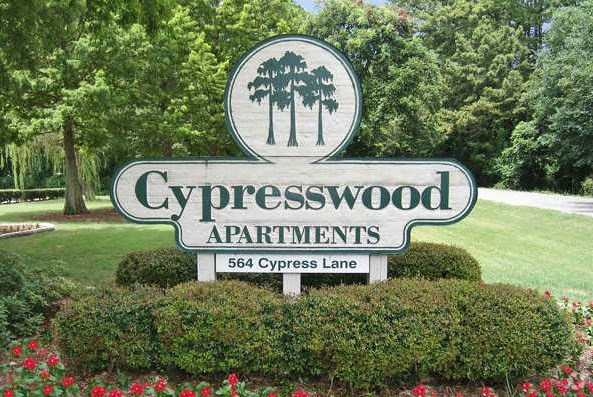 a sign for cypresswood apartments in front of a lawn and trees