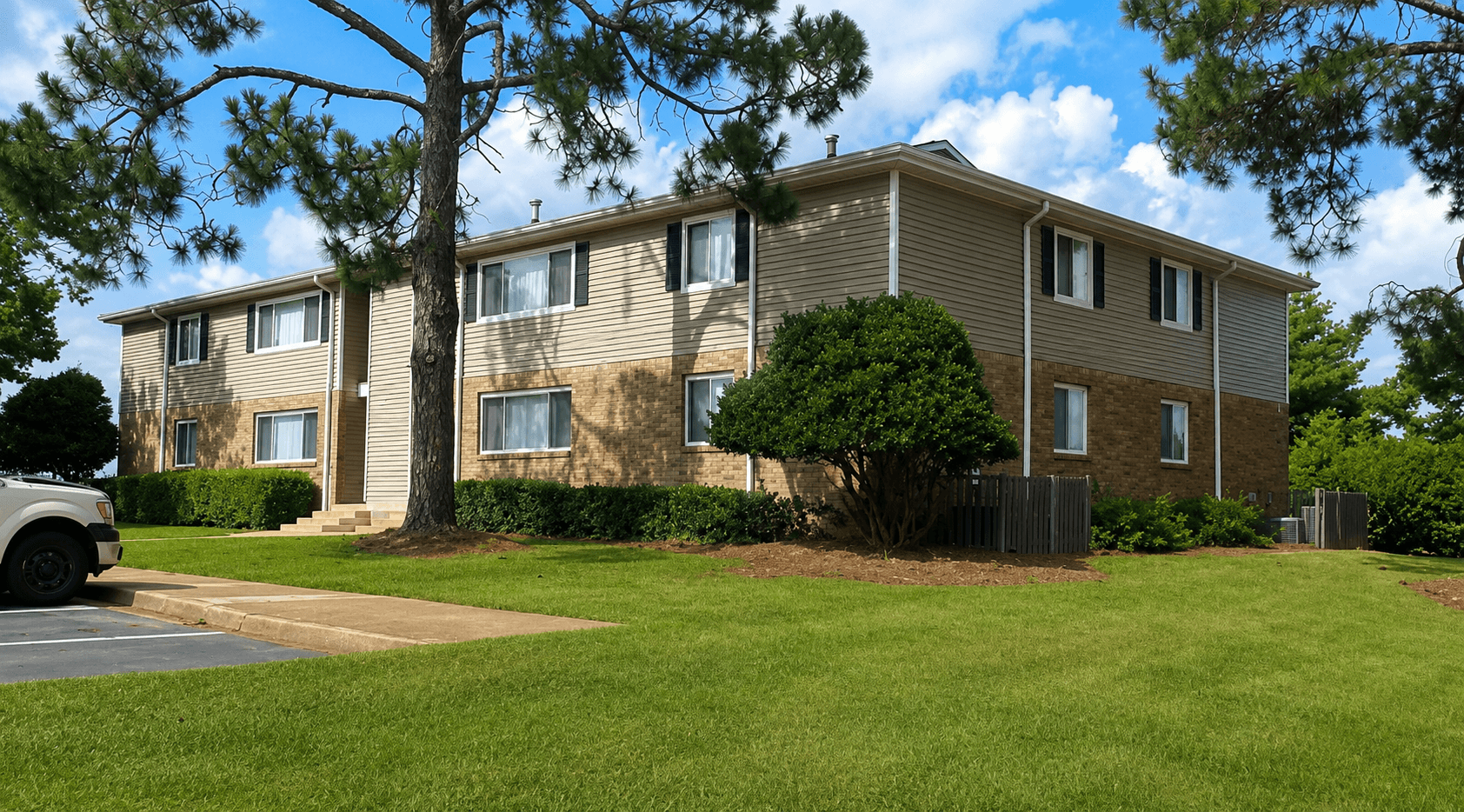 A building with a brown and beige exterior is surrounded by a green lawn and trees.