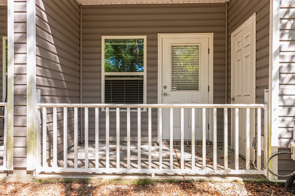 the front porch of a gray house with a white railing and a white door
