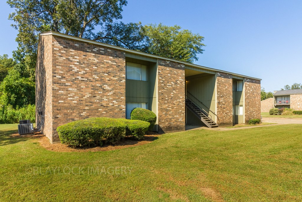 a small brick building with green shutters and a grassy lawn
