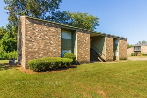a small brick building with green shutters and a grassy lawn
