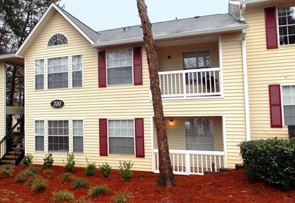 A yellow house with red shutters and a tree in front.