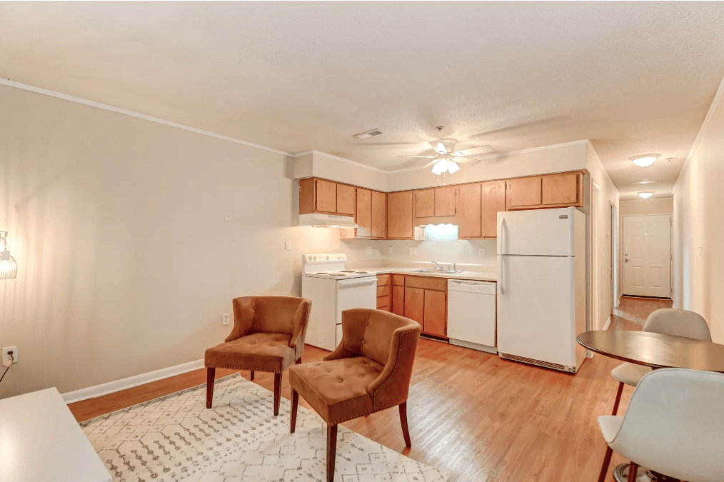 a living room with two chairs and a kitchen with white appliances