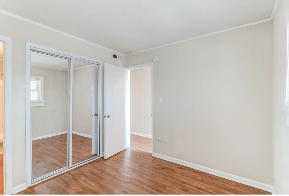 a bedroom with mirrored closet doors and a hard wood floor