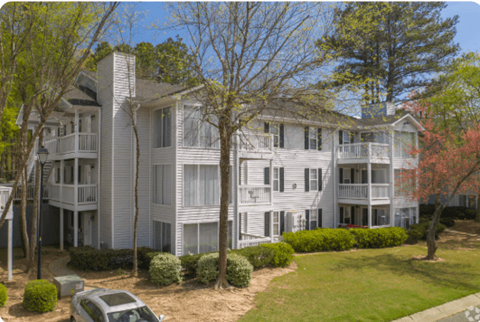 A white two story apartment building with a car parked in front.
