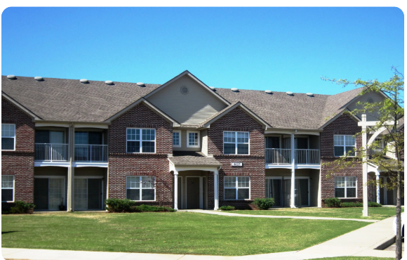 A large brick apartment building with a green lawn in front.