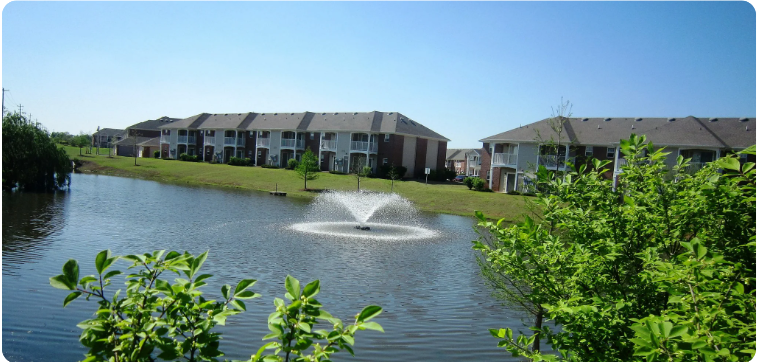 A fountain in the middle of a lake surrounded by houses.