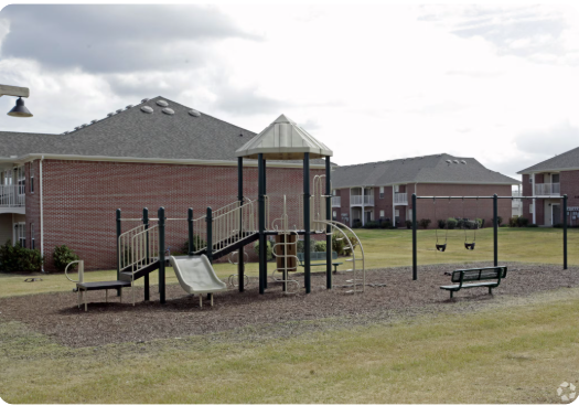 A playground with a slide, swings, and a bench in front of a building.