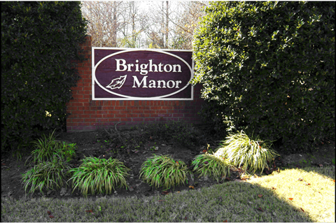 A sign that says Brighton Manor in front of some bushes.