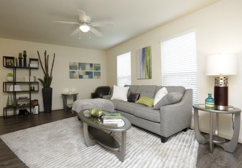 A living room with a grey couch, a white rug, and a ceiling fan.