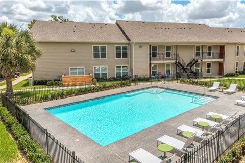 A swimming pool surrounded by a black fence and lounge chairs.