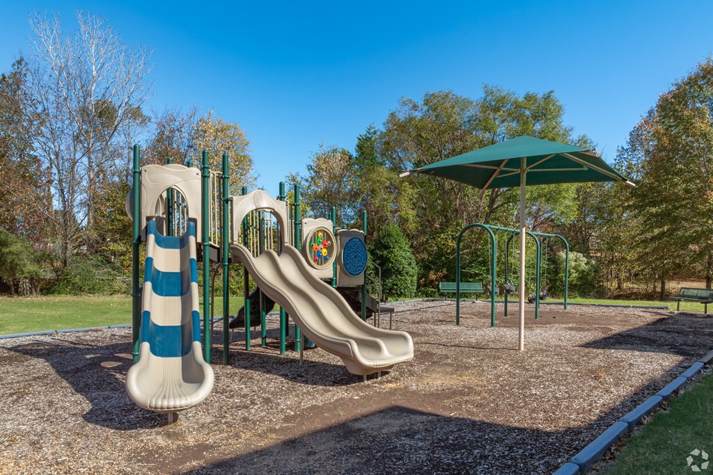 A playground with a slide and a green umbrella.