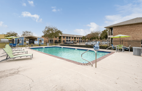 A pool with a sun lounger and umbrella in front of a building.