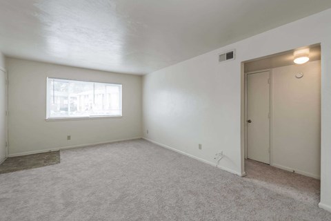 A room with a carpeted floor, a window, and a door.