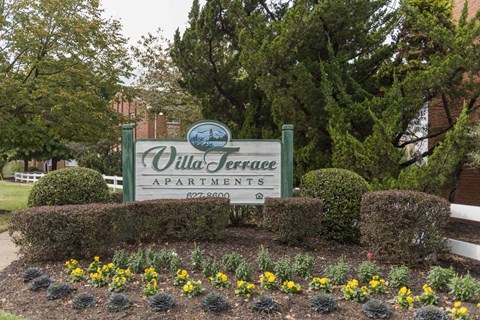 A sign for Olde Terrace Apartments is surrounded by bushes and flowers.