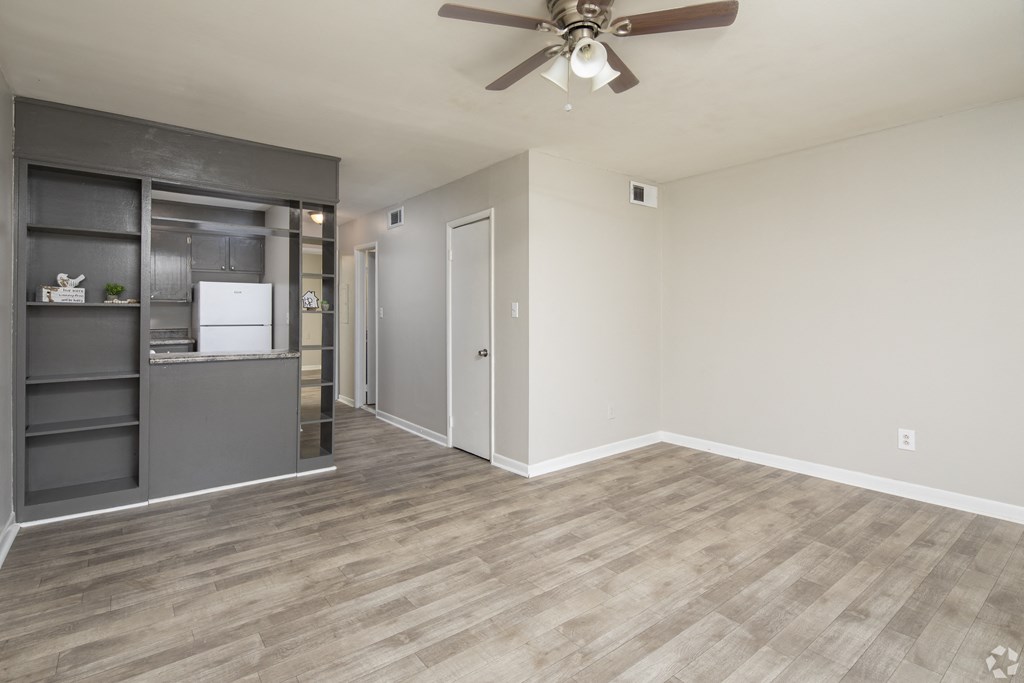 an empty living room with a ceiling fan and a kitchen