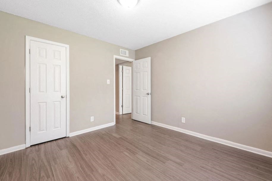 an empty living room with white doors and wood flooring