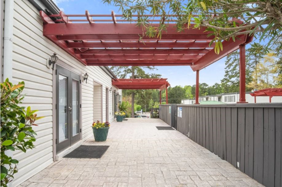 the covered walkway of a white house with a red roof