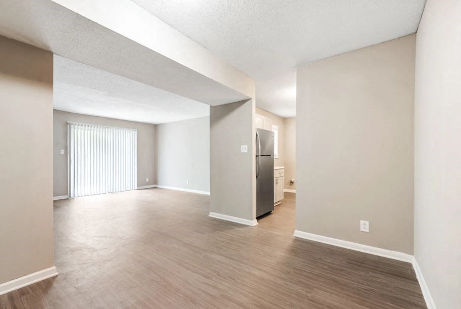 an empty living room with wood flooring and a stainless steel refrigerator