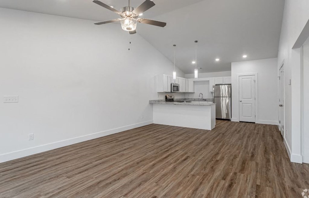 a living area with a ceiling fan and a kitchen in the background