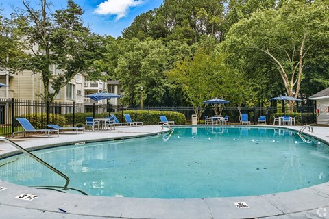 A swimming pool surrounded by trees and chairs.