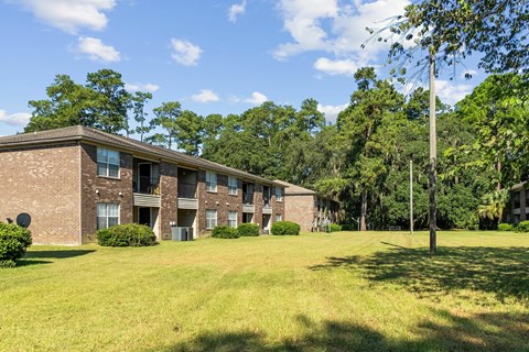 A grassy area in front of a brick building with trees in the background.