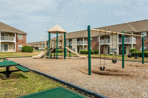 A playground with swings and a slide in front of apartment buildings.
