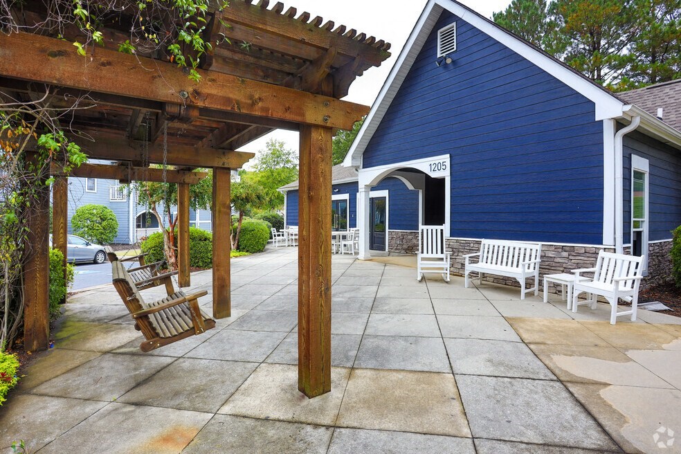 a covered patio in front of a blue house with white rocking chairs