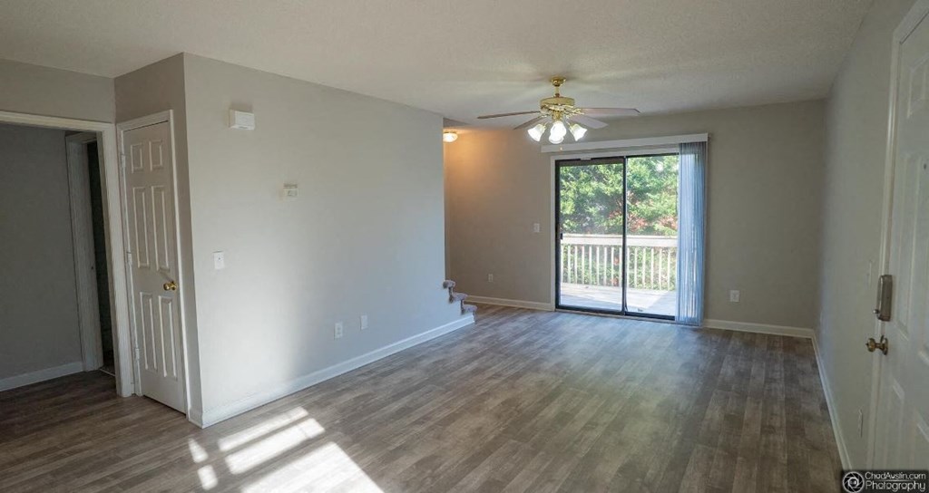an empty living room with a sliding glass door and a ceiling fan