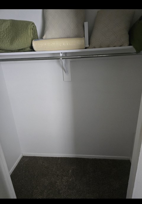 A white shelf with a green towel and two pillows on it.