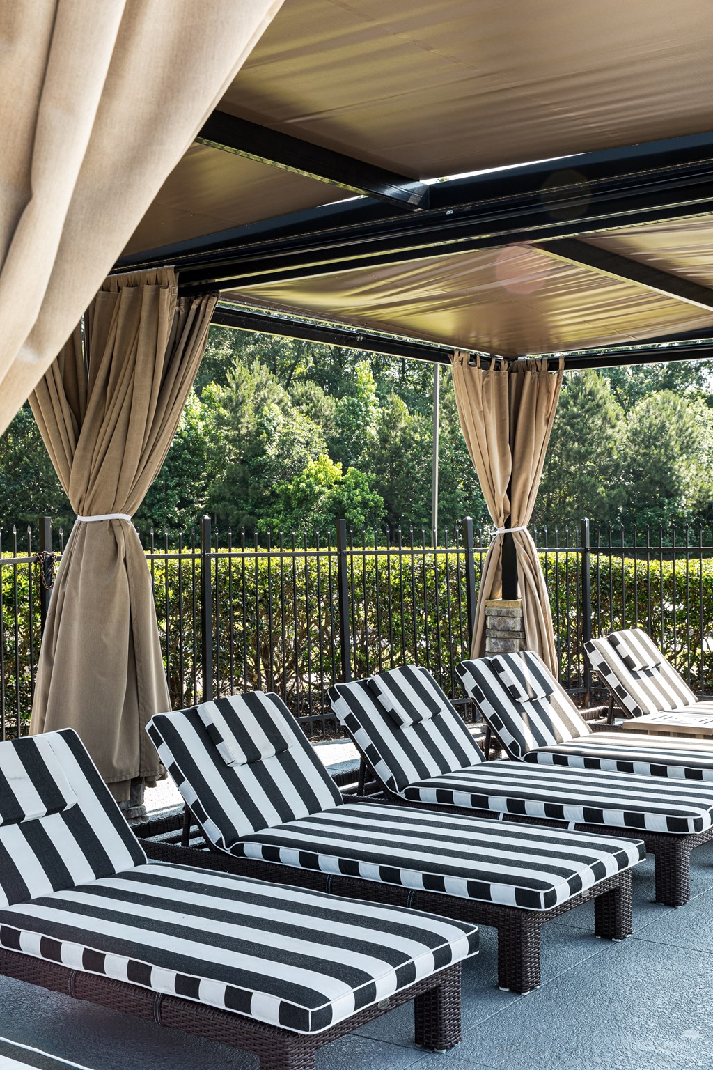 an outdoor lounge area with black and white striped lounge chairs and beige curtains