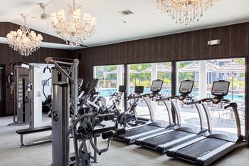 a room with a row of treadmills and two chandeliers hanging from the ceiling