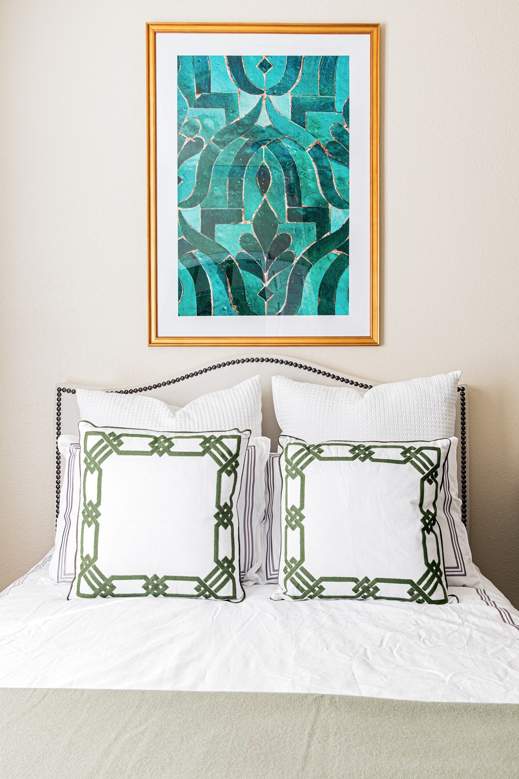 a bedroom with white bedding and a turquoise painting hanging above the bed