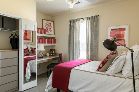 a bedroom with a bed with a red blanket and pillows and a desk with a computer