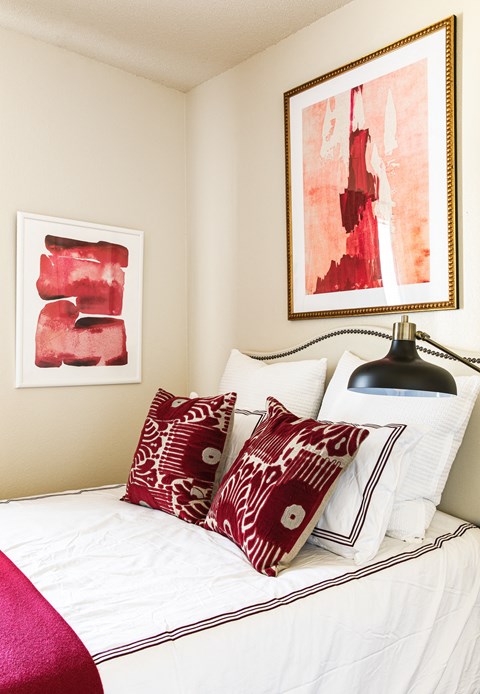 a bedroom with red and white pillows and artwork on the wall
