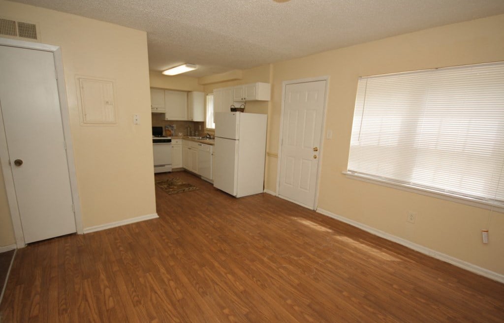 an empty kitchen and living room with wood flooring and white appliances