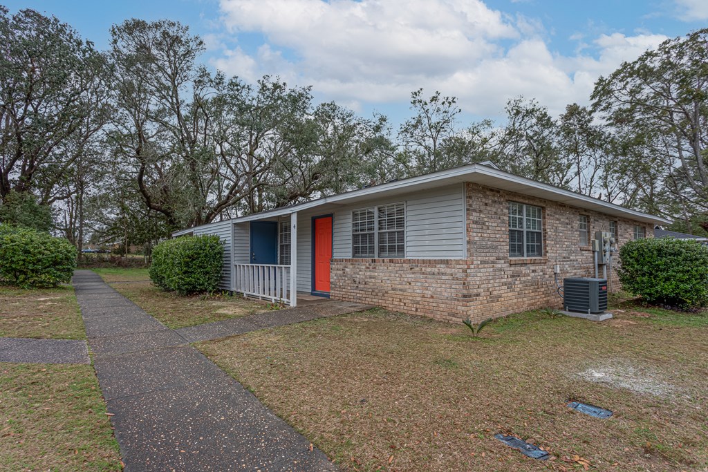 a small white and brick home with a red door