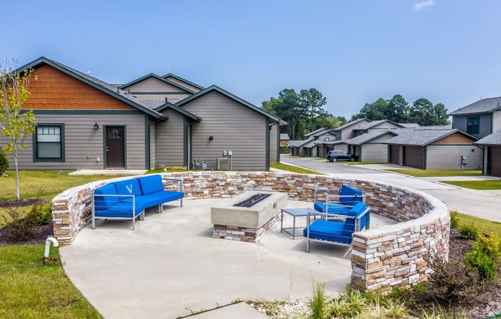 a fire pit with blue lounge chairs on a concrete patio in front of a row of houses