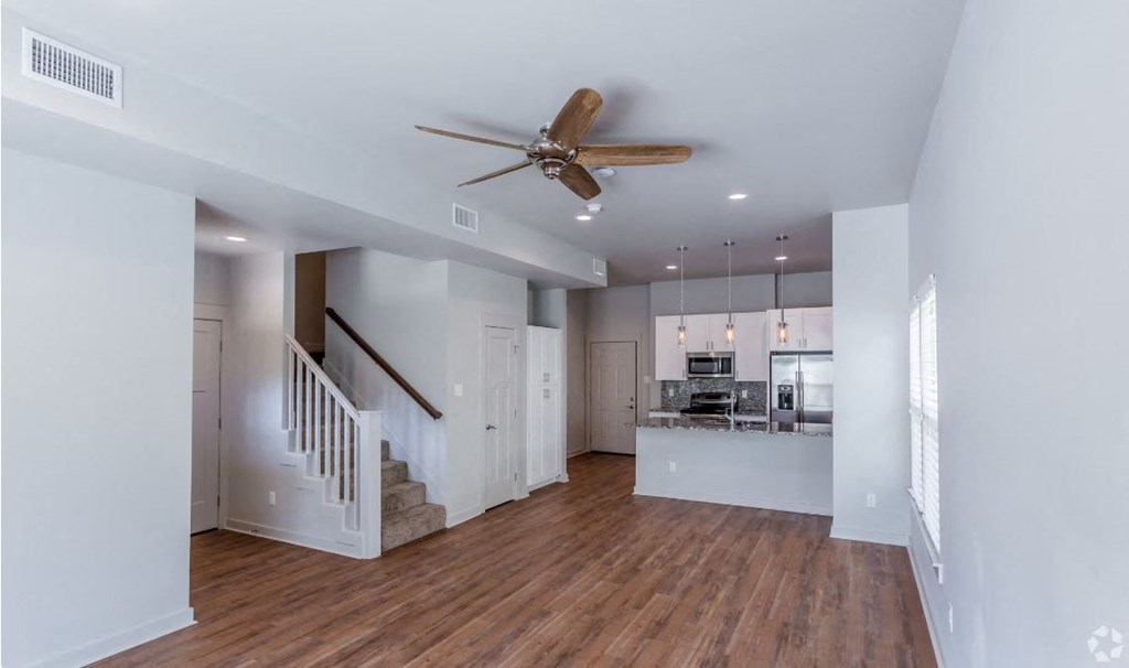 a living room with a ceiling fan and a kitchen in the background