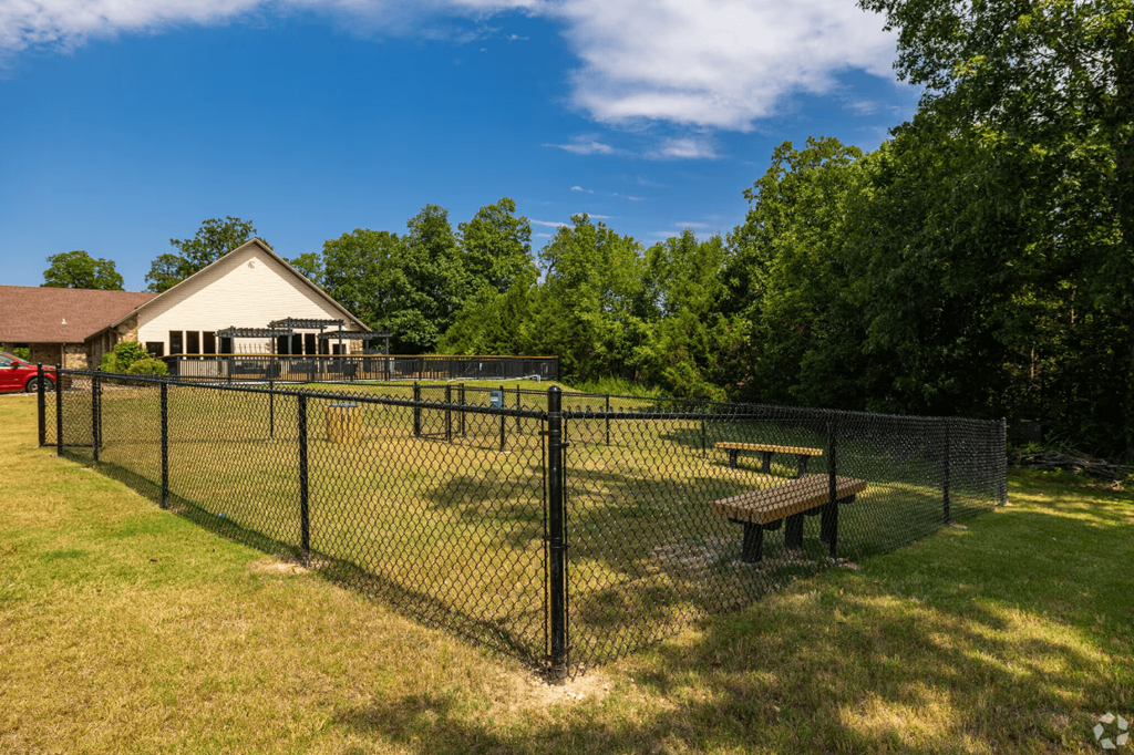 a fenced in dog park with a picnic table and a house in the background