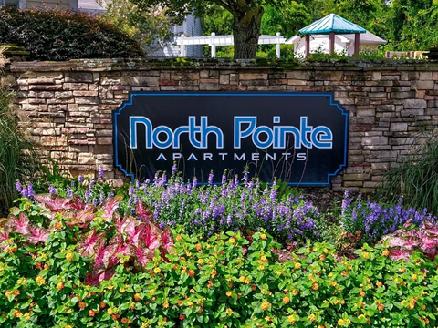 A sign for North Pointe Apartments is surrounded by flowers.