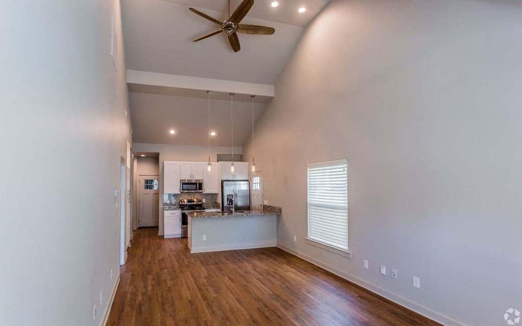 a living room with a ceiling fan and a kitchen in the background