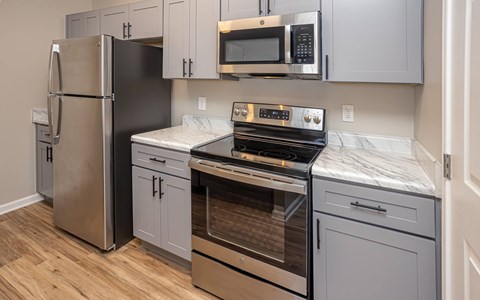 A kitchen with a stainless steel refrigerator, microwave, oven, and cabinets.