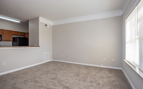 A spacious living room with a carpeted floor and a window on the right side.