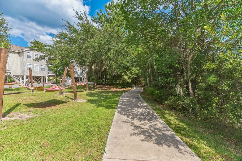 a sidewalk leading to a park with a hammock and trees