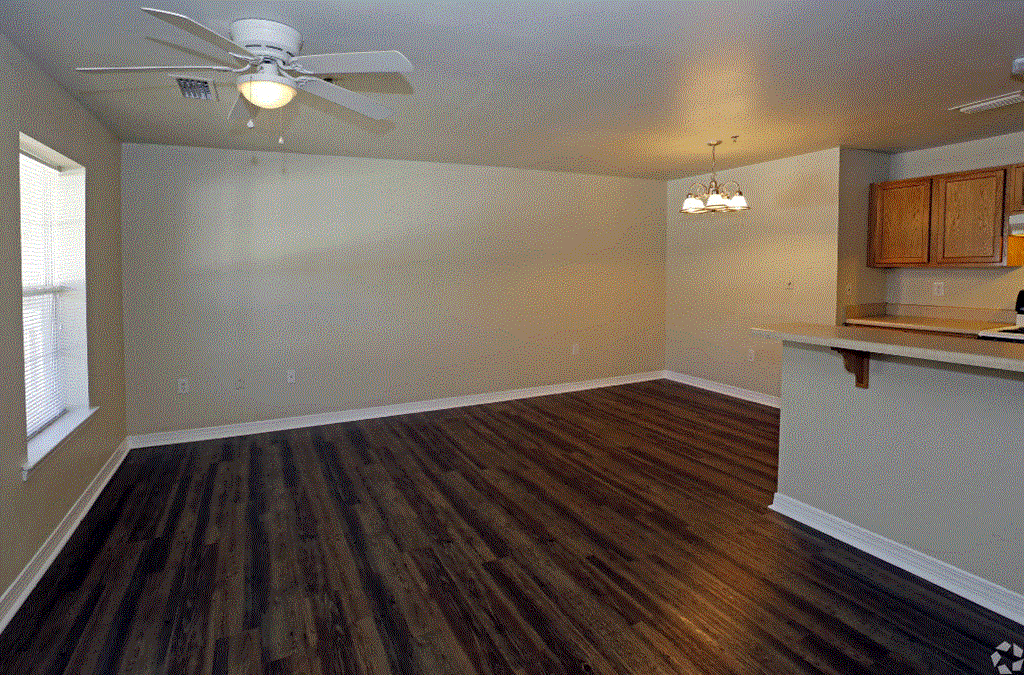 an empty living room with a kitchen in the background
